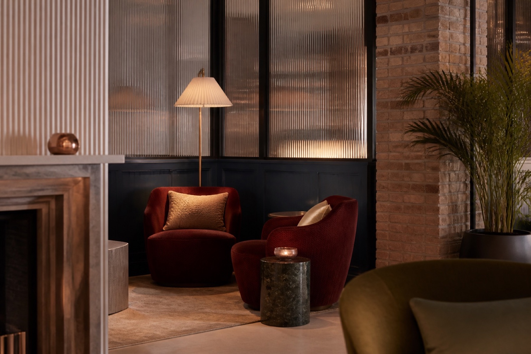 Hoek van een hotelkamer met rode fauteuil, schemerlamp en bakstenen muur